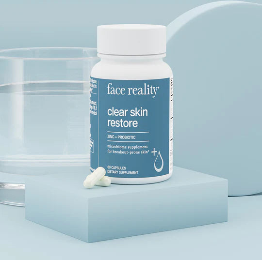 A bottle of 'face reality clear skin restore' supplement with two capsules placed in front, against a white background.