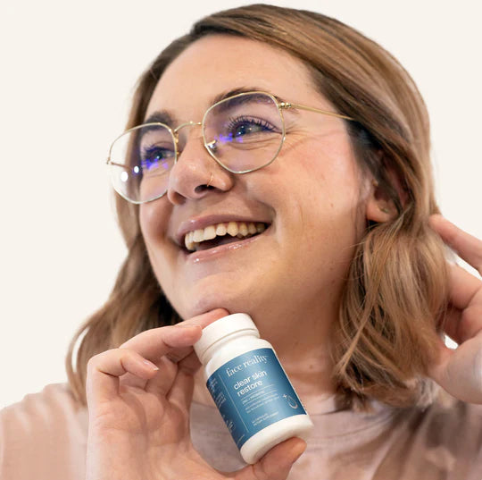 A bottle of 'face reality clear skin restore' supplement with two capsules placed in front, against a white background.