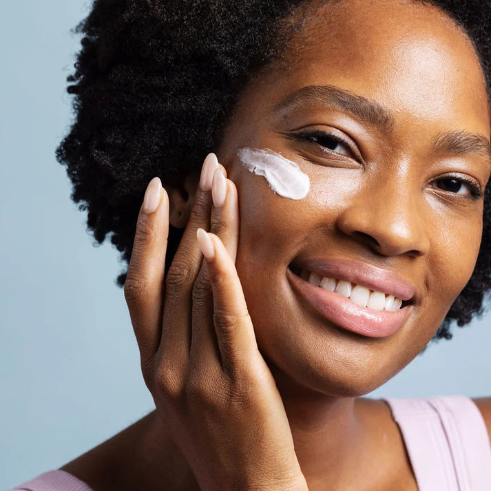 Woman applying cream to her face with a blue background