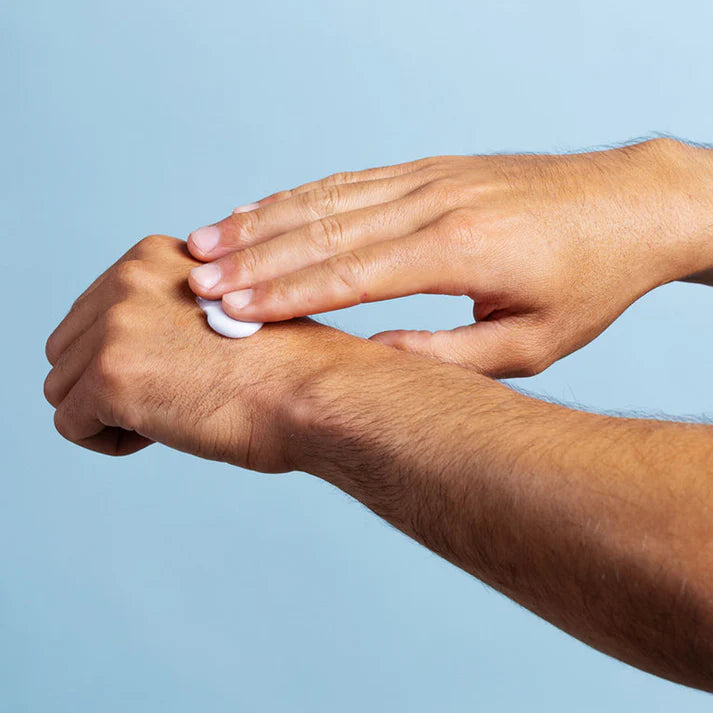 Hand applying cream to another hand against a light blue background