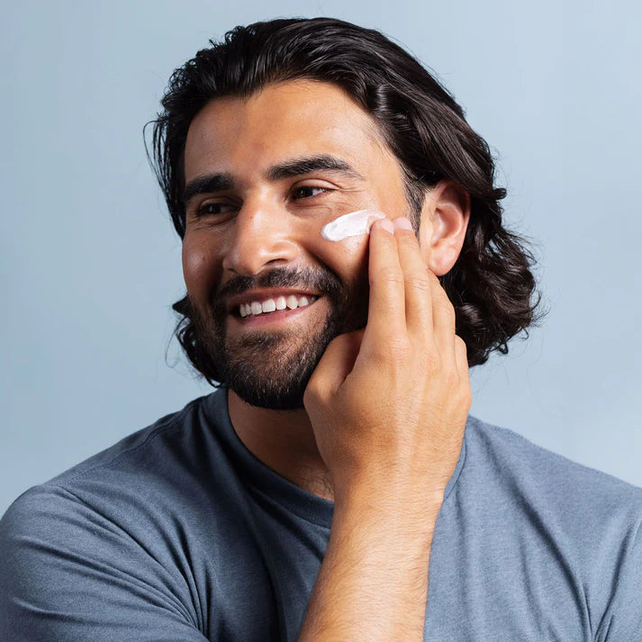Man applying cream to his face against a light blue background